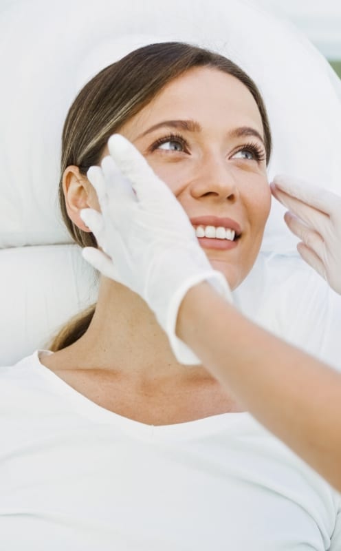 Smiling woman receiving a cosmetic skin treatment from a gloved provider