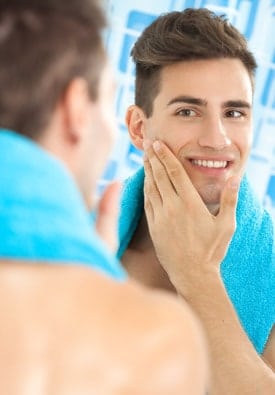 young man looking at his face in the mirror after getting a skincare treatment